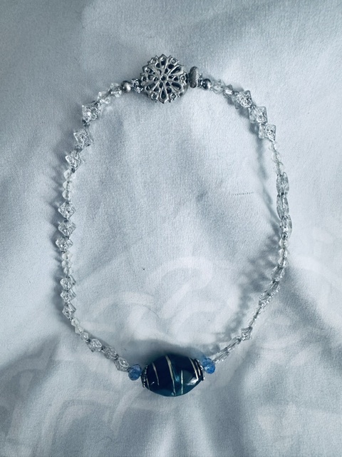 Collier avec grosse perle fantaisie de qualité en cadrée par deux perles en verre et perles fantaisies blanches et argentée. Terminé par un joli fermoir argenté.